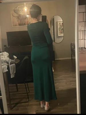 Grön långärmad långklänning - Säljer en snygg grön långklänning med lång ärm och v-ringad hals. Klänningen har en figurnära passform och är tillverkad i ett mjukt, stretchigt material som sitter skönt mot kroppen. Perfekt för dig som gillar stilrena och enkla plagg med lite edge.