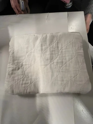 Vit quiltad datorväska med dragkedja - Säljer en stilren vit datorväska med quiltat mönster och praktisk dragkedja. Väskan är rektangulär och har ett mjukt, vadderat tyg på utsidan och slät insida. Perfekt för att skydda din laptop när du är på språng.