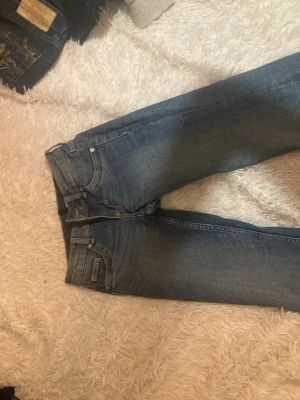 Blå jeans med raka ben - Snygga blå jeans med klassisk femficksdesign och raka ben. Jeansen har normal passform och är tillverkade i ett slitstarkt denimtyg. Färgen är mellanmörkblå och de har en enkel look utan synliga mönster eller detaljer. Perfekta för dig som gillar en clean och tidlös stil.