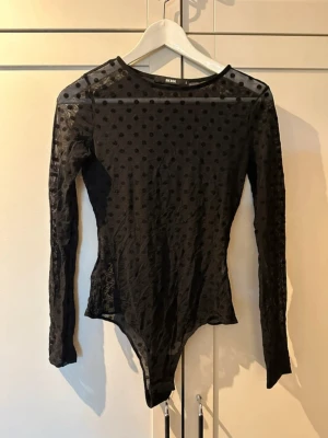 Svart prickig mesh bodysuit från Bik Bok - Säljer en svart långärmad bodysuit från Bik Bok i meshmaterial med prickigt mönster. Toppen har rund hals och är figurnära med transparenta partier. 
