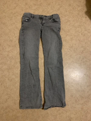 Grå bootcut jeans från Gina Tricot - Snygga grå jeans från Gina Tricot i storlek 170. Modellen har bootcut-ben och klassisk femficksdesign med dubbla knappar fram. Materialet är jeans och bakfickan har en cool stjärndetalj. Perfekt för dig som gillar en avslappnad stil.