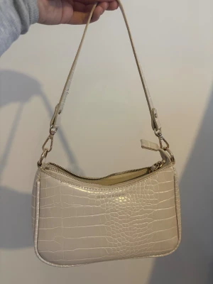 Beige axelväska från iDeal of Sweden - Snygg beige axelväska från iDeal of Sweden med croco-mönster och guldfärgade detaljer. Väskan har en smidig dragkedja upptill.