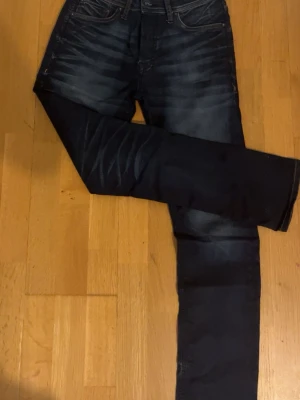 Mörkblå jeans från Jack & Jones - Snygga mörkblå jeans från Jack & Jones med klassisk femficksdesign och kontrastsömmar. Jeansen har en rak passform och subtila slitningar på framsidan och baksidan av benen. Materialet är robust denim med skön känsla och läderpatch bak i midjan.