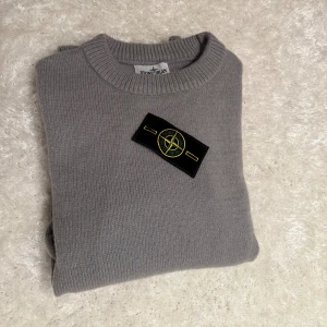 Grå stickad Stone Island tröja - Snygg grå stickad tröja från Stone Island med klassisk rund hals och ribbade muddar. Tröjan har den ikoniska Stone Island-patchen på vänster ärm och är tillverkad i mjukt material som känns skönt mot huden. Perfekt nu för höst/vintern. Tröjan är inprincip helt ny endast testad.