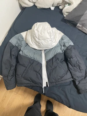 Nike pufferjacka XL i svart och vitt - Säljer en fet pufferjacka från Nike i storlek i S.Jackan har en snygg färgblockad design i svart, grått och vitt, med huva och dragkedja framtill. Perfekt för kalla dagar och har två sidofickor. Materialet är polyester och jackan är riktigt varm.