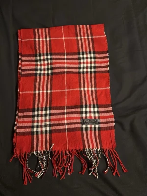 Rutig röd Burberrys halsduk  - Säljer en klassisk rutig halsduk från Burberrys i rött, svart och vitt. Halsduken är tillverkad i 100% lammull och har fransar längst ner. Perfekt för dig som gillar tidlös design och vill sticka ut med ett ikoniskt mönster.                     Fraktar inom 24h. Hör av dig vid frågor eller funderingar 😃🤩👍
