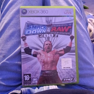 WWE SmackDown vs Raw 2007 (Xbox 360) - WWE SmackDown vs Raw 2007 till Xbox 360. Omslaget och fodralet är i gott skick med mindre tecken på normalt slitage. Ett populärt wrestling-spel med realistisk grafik och många spelbara karaktärer. Perfekt för fans av WWE och sportspel.