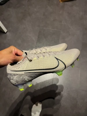 Nike Vapor 360 fotbollsskor i beige - Säljer ett par Nike Vapor 360 fotbollsskor i beige med svart swoosh. Skorna har snörning och en stickad ovandel för grym passform. Sulan är utrustad med limegröna dobbar och lila detaljer för extra grepp på planen. Perfekt för dig som vill ha stil och funktion på träningen.