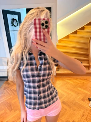 Rutig kortärmad skjorta i blått och vitt - Säljer en kortärmad skjorta med snyggt rutigt mönster i blått och vitt. Skjortan har knappar framtill och en figurnära passform som ger en fräsch och ungdomlig vibe. Perfekt för dig som gillar klassisk stil med en modern twist.