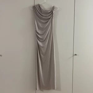 Champagnefärgad långklänning från H&M - Säljer en elegant långklänning i champagnefärg från H&M Divided, storlek S. Klänningen har oneshoulder-design med draperad effekt och mjukt, glansigt material som ger en lyxig känsla. Perfekt för dig som gillar stilrena och moderna plagg. Oanvänd