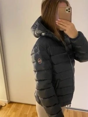 Mörkblå Colmar pufferjacka med huva - Säljer en mörkblå pufferjacka från Colmar med huva och dragkedja framtill. Jackan har quiltad design, två fickor med dragkedja och en snygg logga på ärmen. Perfekt för kyliga dagar och riktigt skön att bära.