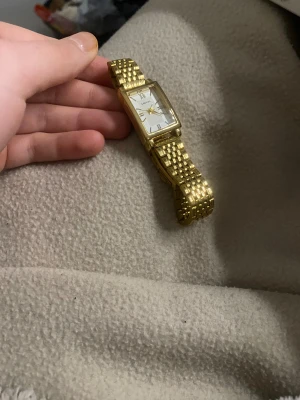 Guld klocka  - Bilderna visar en guldfärgad klocka med rektangulär urtavla och metallarmband