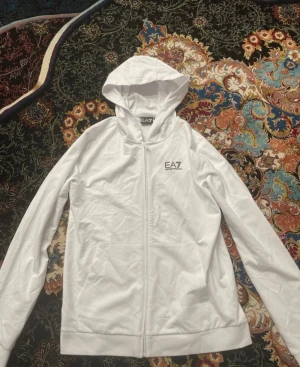 EA7 Hoodie - Helt ny vit EA7 hoodie aldrig använd!  Letar du efter en snygg och bekväm hoodie? Då är denna vita EA7 hoodie perfekt! 	•	Storlek: 170 CM 	•	Helt ny  Pris: Börjar med 500kr Vi kan snacka om priset  