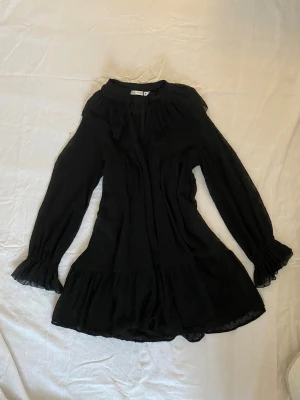 Svart volangklänning från Zara XS - Supersöt svart kortklänning från Zara med volangdetaljer och långärmade ärmar med rynkade muddar. Klänningen har en lätt transparent känsla och diskret prickigt mönster i tyget. Perfekt inför julen eller nyår💗 jag har endast testat den.