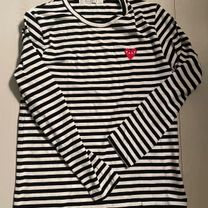 Randig långärmad tröja Comme des Garçons - Säljer en svartvit randig långärmad tröja från Comme des Garçons Play. Tröjan har ett broderat rött hjärta med ögon på bröstet och är gjord i mjuk bomull. Perfekt för dig som gillar clean streetstyle med en twist.