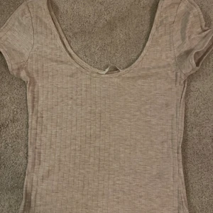 Beige ribbat sett med topp och byxa - Säljer en beige ribbat sett med kortärmad topp och matchande vida byxor. Setet har en ljus ton och är tillverkat i mjukt, stretchigt material som ger en skön passform. Toppen har en djup rundad halsringning och byxorna är långa med rak siluett. Toppen är i nyskick och byxorna är oxå i nyskick bortsätt ifrån att de kommit fläckar längs ner på benen som man kan se på bild 3. Inte så synliga 