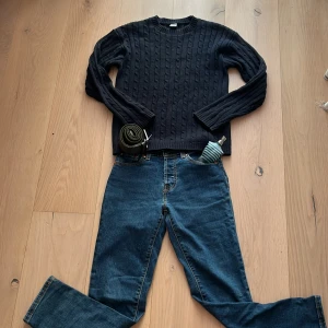 Mörkblå kabelstickad tröja - Snygg mörkblå kabelstickad tröja med rund hals och långa ärmar. Tröjan har ett klassiskt mönster med flätade detaljer och ribbade muddar vid ärmslut och nederkant. Perfekt för dig som gillar stilren och enkel design.