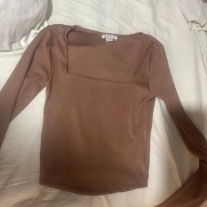 Brun långärmad topp från Amisu - Säljer en brun långärmad topp från Amisu med fyrkantig ringning. Toppen är i mjukt material och har en enkel, stilren design som passar perfekt till jeans eller kjol. Snygg och basic för dig som gillar minimalistisk stil.