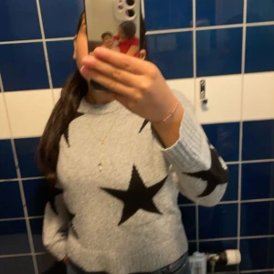 Grå stickad tröja - Säljer en grå stickad tröja med stora svarta stjärnor som mönster. Tröjan har rund hals och långa ärmar, perfekt för dig som gillar en cool och avslappnad stil. Passar till jeans och sneakers för en chill look.