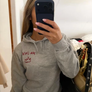 Grå hoodie med röd text Ma Chérie - Grå hoodie med huva och snörning, dekorerad med röd texten 'MA CHÉRIE' och en krona både fram och bak. Mjuk och skön, perfekt för chill dagar. Klassisk passform och ribbade muddar vid ärmslut och midja. Storlek 158/164 passa mkg som bruka ha S