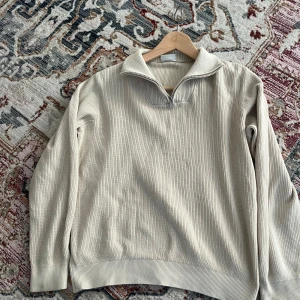 Beige stickad half zip-tröja Kappahl - Säljer en beige stickad tröja från Kappahl med ribbad struktur och snygg krage med half zip-dragkedja. Tröjan har lång ärm och är perfekt för lager-på-lager under hösten eller vintern. Enkel och stilren design som passar till allt.