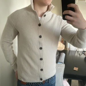 Beige merinoull stickad cardigan - As fet stickad beige j.lindeberg cardigan. Perfekt till kallare väder. Modellen är 180cm, 73kg. 55%-merinoull, 45%-bomull. Priset går såklart att diskutera!