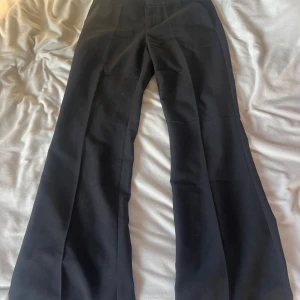 Svarta bootcut kostymbyxor - Snygga svarta kostymbyxor med bootcut-snitt och hög midja. Byxorna har en klassisk rak passform upptill och blir vidare nedtill, vilket ger en trendig siluett. Perfekta att matcha med en cool topp eller hoodie för en stilren look.