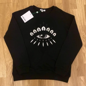 Svart Kenzo sweatshirt   - Svart sweatshirt från Kenzo med ikoniskt broderat logga i silver och vitt.                                                 Materialet  är mjuk bomull och passformen är normal. Perfekt för dig som gillar märket!
