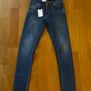 Tiger of Sweden blå slim jeans W29 L32 - Snygga blå jeans från Tiger of Sweden med skinny passform och klassisk femficksdesign. Jeansen har en mörk tvätt med lätt slitning och är tillverkade i stretchigt denim för skön komfort. Perfekt för dig som gillar en smal siluett och stilren look. Helt nya med prislapparna kvar