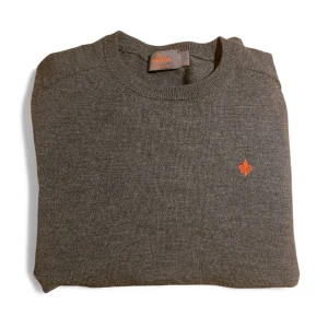 Morris tröja merinoull  - Snygg mörkgrå stickad tröja från Morris i 100% merinoull. Klassisk rund hals och orange broderad logga på bröstet ger en clean och stilren vibe. Perfekt för dig som gillar enkel design med en twist. Priset är inte hugget i sten.👍