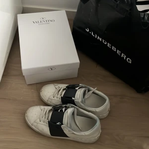 Valentino Garavani Open sneakers vit/svart - Säljer ett par Valentino Garavani Open sneakers i vitt skinn med bred svart läderdetalj över vristen. Klassisk rund tå, platt sula och snörning. Kommer med originalkartong och dustbag. Perfekt för dig som gillar exklusiva och stilrena sneakers.