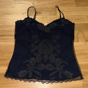 Vintage Mörkblå blommig linnetopp Monsoon - Vintage Supersöt mörkblå linnetopp från Monsoon med tunna axelband, broderade blommor framtill och vågig spetskant nertill. Toppen har knappar i ryggen och är gjord i ett tunt, lätt material som känns luftigt och elegant.