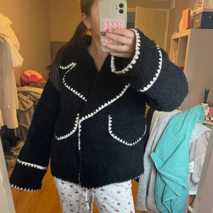 Svart teddyjacka från Object, stl 34 - Mysig svart teddyjacka från Object med vita virkade detaljer längs kanter, fickor och ärmslut. Jackan har en lite oversized passform, stora slag och två framfickor. 