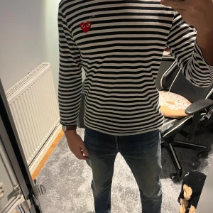 Randig långärmad tröja Comme des Garçons - Säljer en svartvit randig långärmad tröja från Comme des Garçons Play med det ikoniska röda hjärtat broderat på bröstet. Tröjan är i mjuk bomull och har en normal passform. Perfekt för dig som gillar stilrena och coola detaljer.