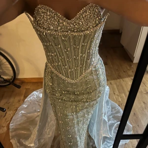 Bröllopsklänning  - Magisk långklänning i ljus champagnefärg med glittriga pärlor och stenar över hela livet och kjolen. Klänningen har en figurnära passform, axelbandslös design och en vacker släp. Perfekt för bal eller nyår, med lyxig känsla och detaljer som verkligen sticker ut. Storlek xs passar även s. (Handmade)