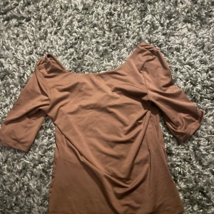 Brun topp med vid urringning från H&M - Säljer en brun topp från H&M i storlek S. Toppen har en vid, rund urringning och halvlånga ärmar. Den är figurnära och tillverkad i mjuk bomullsblandning, perfekt för en enkel och stilren look.
