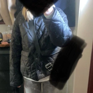 Svart quiltad jacka med bälte - Säljer en svart quiltad jacka har stora fickor framtill. Jackan har lång ärm och stängs med knappar. Perfekt för dig som gillar en stilren och trendig look.