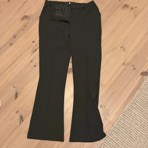 Gröna bootcut byxor från Bubbleroom - Gröna bootcut byxor från Bubbleroom i storlek L. Snyggt skräddade med pressveck och klassisk midja. Materialet är mjukt och stretchigt, tillverkat av 50% återvunnen polyester, 45% polyester och 5% elastan. Perfekt för dig som gillar stilrena och bekväma byxor.