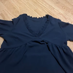 Mörkblå blus med spetsdetalj - Mörkblå blus med v-ringning och fina spetsdetaljer längs halsen. Perfekt för dig som gillar stilrena och eleganta plagg