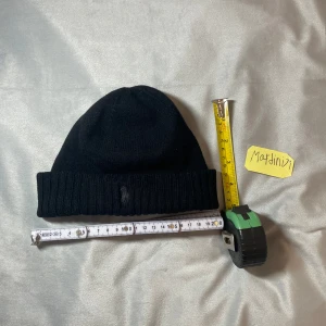 Svart ullmössa från Polo Ralph Lauren - Klassisk svart mössa från Polo Ralph Lauren i 100% ull. Mössan har ribbad uppvikning och den ikoniska broderade Polo-loggan framtill i svart. Är ganska liten storlek passar ett barn typ i 10år åldern,Den är stressig!Den är gjort att vara lite uppåt så typ halvvägs till öronen. Perfekt för kalla dagar och enkel att matcha med olika outfits. Stressig! Passar dig med litet huvud.Den är helt oanvänd.