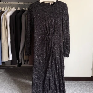 Svart glittrig långklänning - 🤍Svart långklänning från Nelly med glittriga paljetter över hela klänningen. Den har lång ärm, rund halsringning, dragkedja i ryggen och en slits framtill 🤍