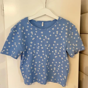 Blommig blå topp från ONLY -  Säljer denna söta baby tee från Only då jag använder den alldeles för sällan, den är max använd 2 gånger.                                                          Den är en storlek S och passar bra på mig som vanligtvis är en 36/38 i toppar. 