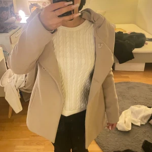 Beige kappa med stor krage - Säljer en snygg beige kappa med stor krage och knäppning framtill. Jackan har en stilren och enkel design med raka linjer och är perfekt för dig som gillar en clean look. Materialet känns mjukt och har en lyxig känsla. Passar dig som vill ha en klassisk vibe.