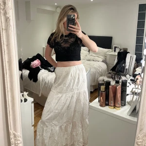 Vit långkjol med broderade blommor - Superfin vit långkjol med broderade blommor och volangdetaljer. Kjolen har en luftig och flowy passform, perfekt för varma dagar. Känns lätt och skön mot huden. Snygg att styla med crop top eller stickad tröja.