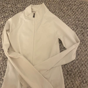 Vit ziptröja från Nelly - Snygg vit långärmad ziptröja från Nelly med hög krage och hel dragkedja framtill. Man kan ha tröjan när man tränar men den är också snygg att ha som en vardaglig tröja. Har använt den några gånger men inga defekter. Nypris 280kr