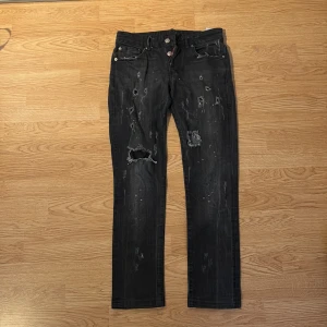 Svarta distressed jeans från Dsquared2 - Snygga svarta jeans från Dsquared2 med slitna detaljer och hål framtill för en edgy look. Modellen har raka ben, klassisk femficksdesign och coola dragkedjor på bakfickorna. Jeansen är tillverkade i jeansmaterial och har en mörk tvätt.