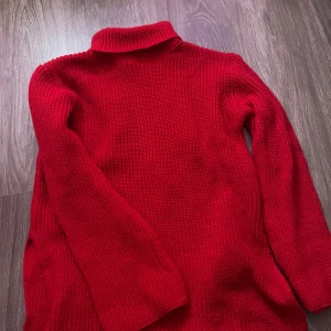 Röd stickad polotröja - Snygg röd stickad polotröja med lång ärm och hög krage. Perfekt för dig som gillar klassisk stil med en färgklick. Tröjan är mjuk och har en grovstickad struktur som gör den extra mysig under kyliga dagar.