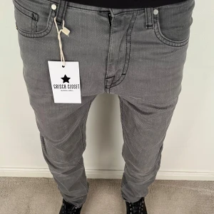 Grå jeans från tiger of sweden med raka ben - Snygga grå jeans från tiger of sweden med klassisk femficksdesign och raka ben. Jeansen har en mörkgrå ton, tydliga sömmar och en patch med T/J-logga bak i midjan. Passar dig som gillar stilrena och enkla jeans med normal passform.