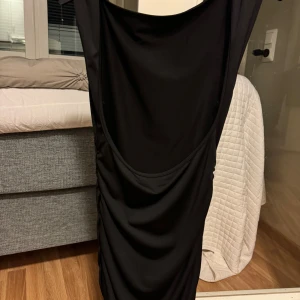 Svart långklänning med öppen rygg - Säljer en svart långklänning i stretchigt material med snygg drapering och djup öppen rygg. Klänningen är ärmlös och har en tight passform med stretchigt material. 