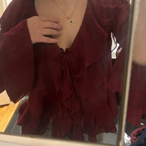 Jul/Nyårs perfekta blus💕 - Supersnygg vinröd blus med volanger och v-ringning. Långa, vida ärmar och knytning framtill ger en romantisk vibe. Tunt, lätt material som faller fint och känns luftigt. Perfekt för dig som vill sticka ut med en elegant och trendig look. Strl M men sitter super på xs/s se bilderna🙂 Superfin till middag fest jul/nyår🥂🥂